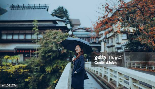 pretty young lady walking along the old town and enjoying the scenics in a japanese zen garden on a rainy day. - garden bridge stockfoto's en -beelden