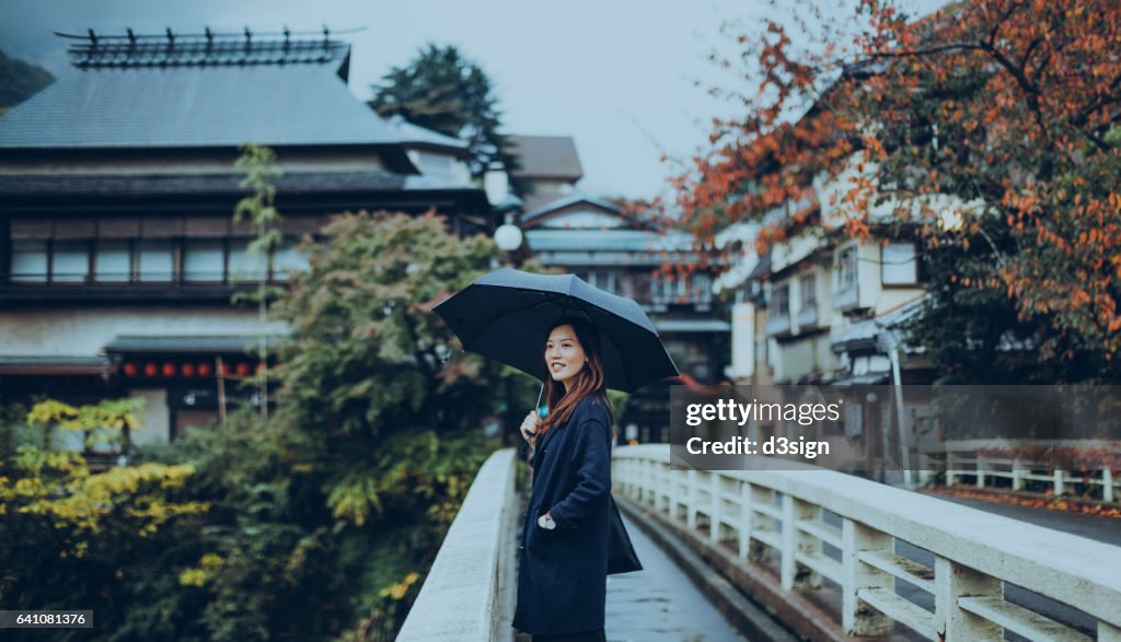 Pretty young lady walking along the old town and enjoying the scenics in a Japanese Zen Garden on a rainy day.