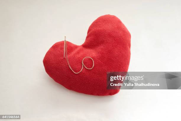 red pillow shaped heart with a needle and thread - broken toy stock pictures, royalty-free photos & images