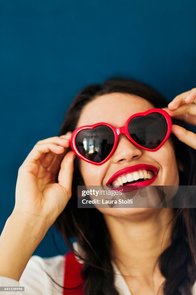 Smiling young woman with red heart shaped sunglasses