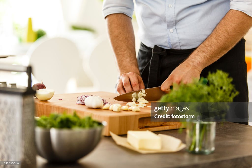 Chef slicing garlic on cutting board