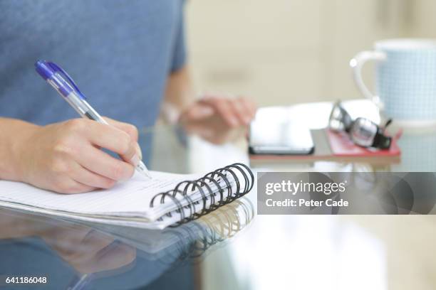 woman sat at table writing list - boodschappenlijst stockfoto's en -beelden