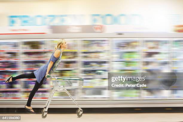 woman riding shopping trolley down aisle - supermarket trolley female stock-fotos und bilder