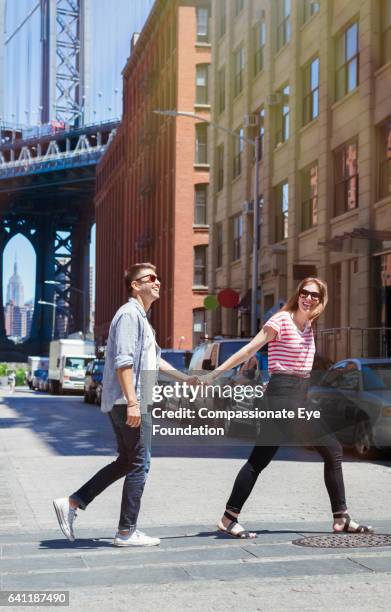 couple walking across city street hand in hand - manhattan bridge stockfoto's en -beelden