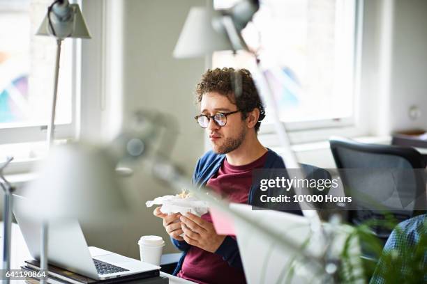 businessman in a start-up office eating breakfast at his workstation - food ready to eat stock pictures, royalty-free photos & images