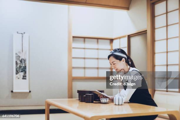 young asian woman using digital tablet and having a  cup of tea in traditional japanese living room - washitsu stock pictures, royalty-free photos & images