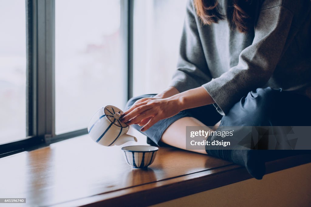 Woman sitting on the windowsill and pouring a cup of tea