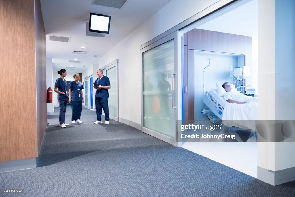 Medical staff talking in corridor, patient in bed in ward