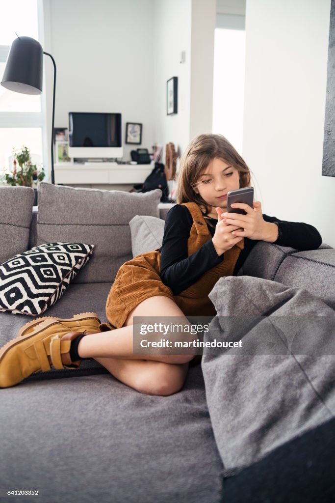 Chica joven disfrutando de móvil tranquilamente en el sofá de la sala de estar.