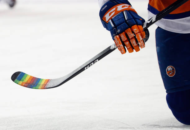 New York Islanders player holds his hockey stick with the blade wrapped in rainbow tape in honor of pride night during pre game warmups prior to an...