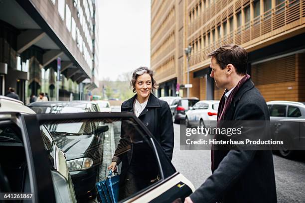 businessman holding door of a taxi for woman - reglas de sociedad fotografías e imágenes de stock