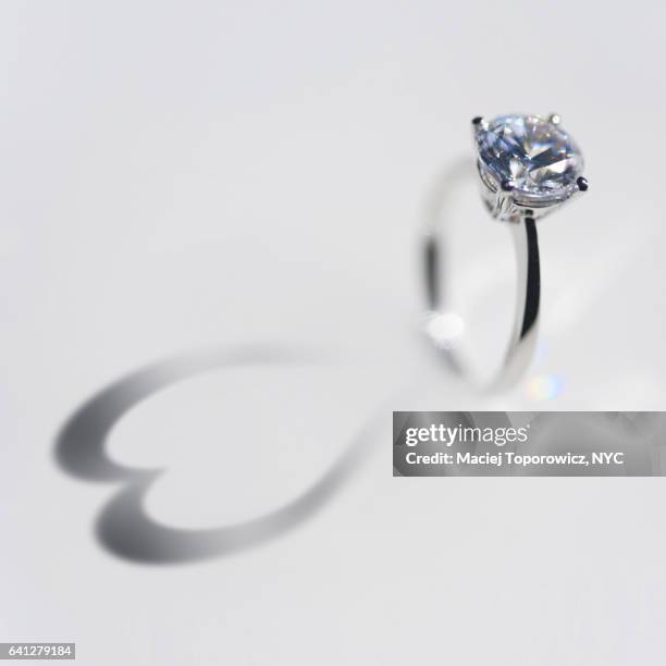 diamond ring with a heart shaped shadow on white background. - ring shaped stock pictures, royalty-free photos & images