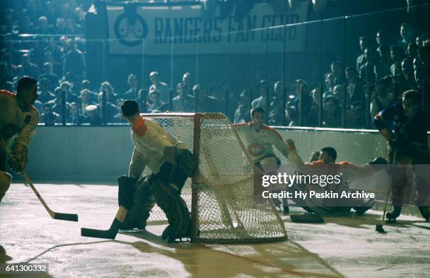 Camille Henry of the New York Rangers skates with the puck around the net as goalie Jacques Plante of the Montreal Canadiens tries to follow the puck...