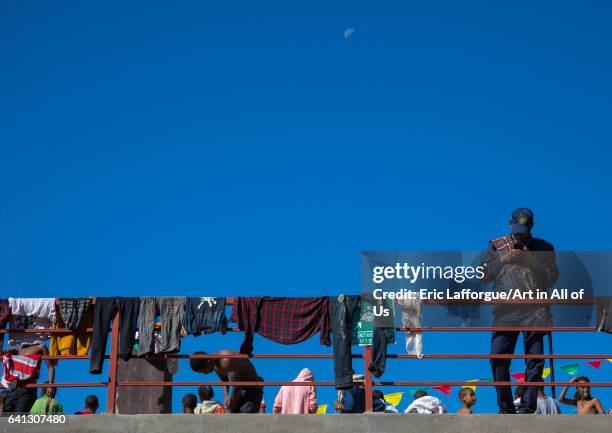 Ethiopian policeman looking at his mobile phone while people dry their clothes after the holy bath during Timkat festival on January 19, 2017 in...