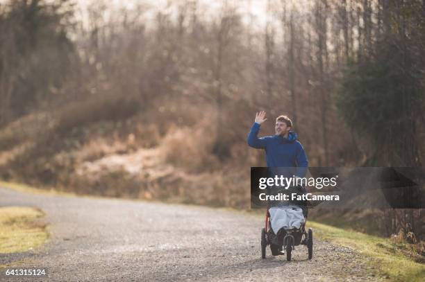 young dad pushing baby stroller outside - three wheeled pushchair stock pictures, royalty-free photos & images