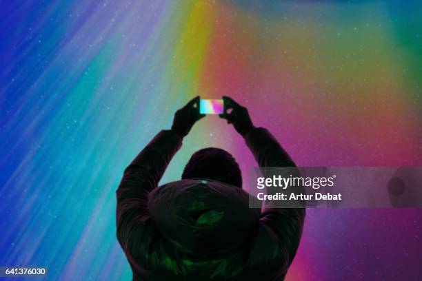 silhouette of a guy taking pictures with smartphone and the beautiful colorful northern lights falling from the sky in iceland in a stunning clear and nice lights with the sky full of stars. aurora borealis. - noorderlicht sterren stockfoto's en -beelden