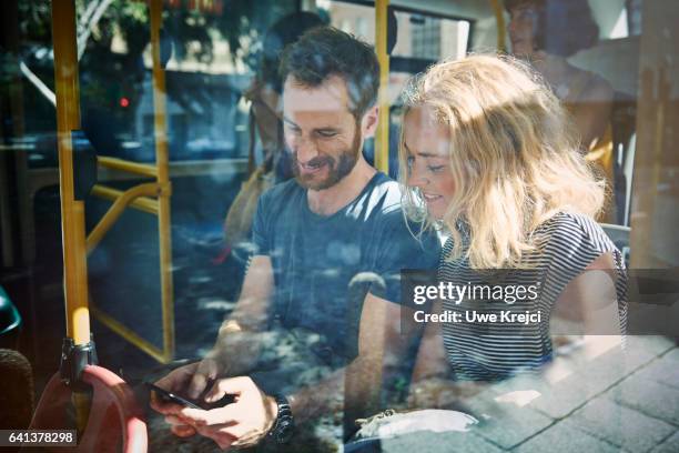 young couple on a bus looking at smart phone - bus window stock pictures, royalty-free photos & images