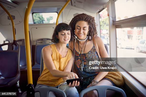 two young women on a bus listening to music on smart phone - two people on bus foto e immagini stock