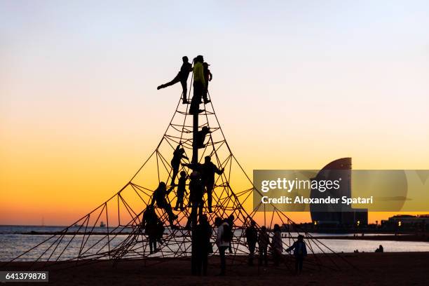 silhouettes of kids on rope playground on barceloneta beach at sunset, barcelona, catalonia, spain - barceloneta fotografías e imágenes de stock