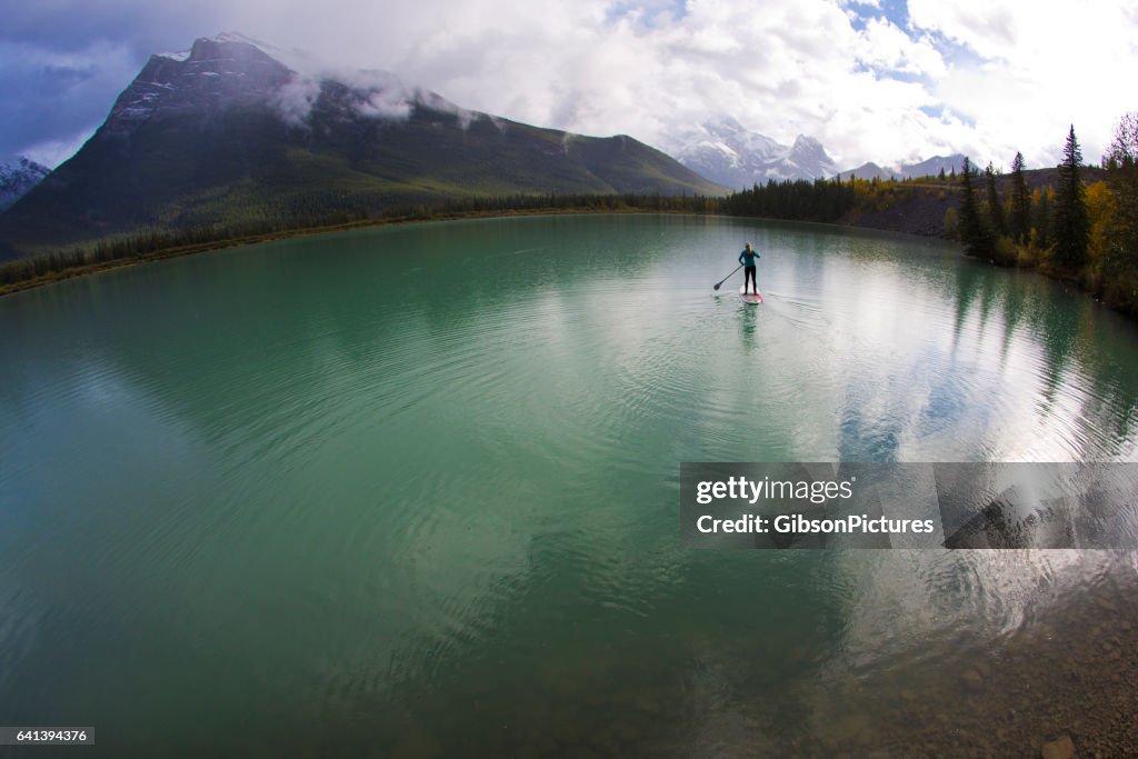 A woman enjoys a stand up paddleboard trip on a lake in the Rocky Mountains of Canada.