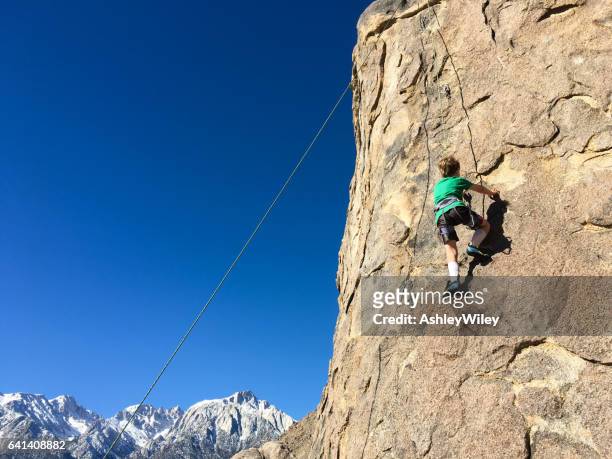 jonge jongen klimmen op het gezicht van een rots in de bergen - extreme hug face stockfoto's en -beelden