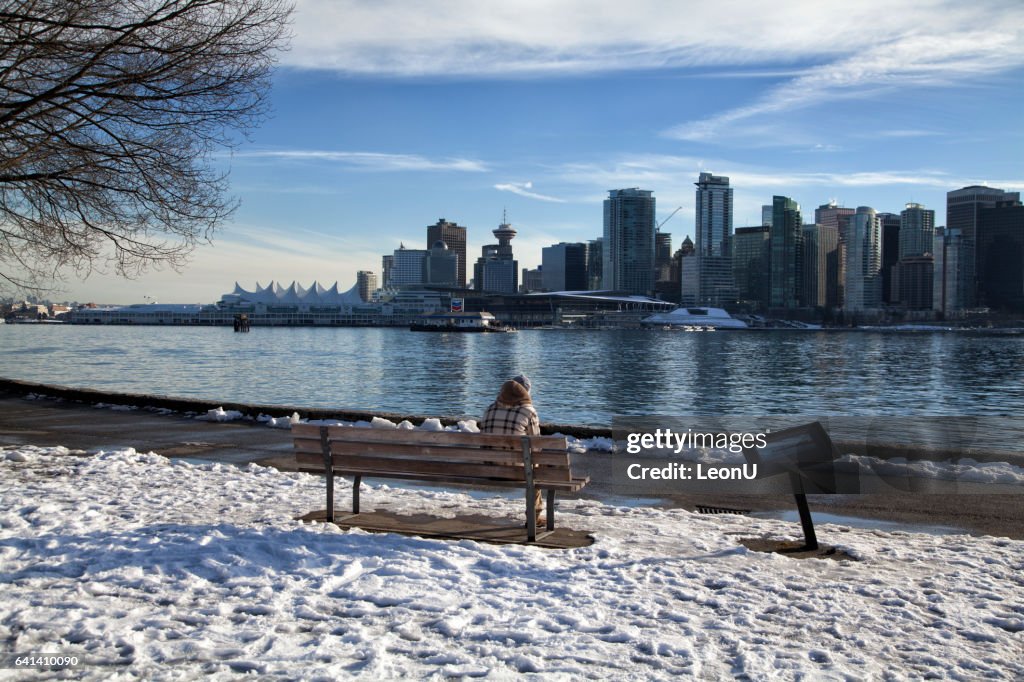 Uomo seduto in panchina godendosi lo skyline di Vancouver