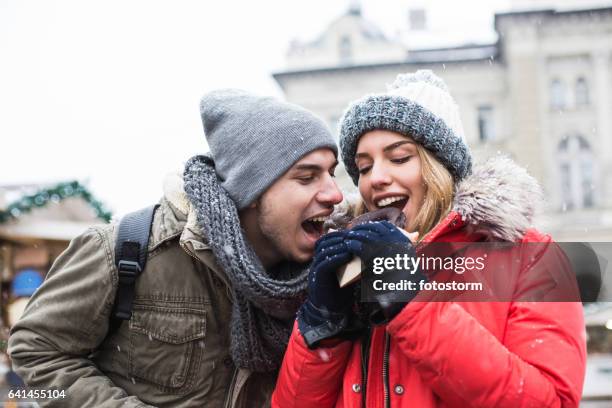 couple sharing chocolate donut at christmas market - chocolate tasting stock pictures, royalty-free photos & images