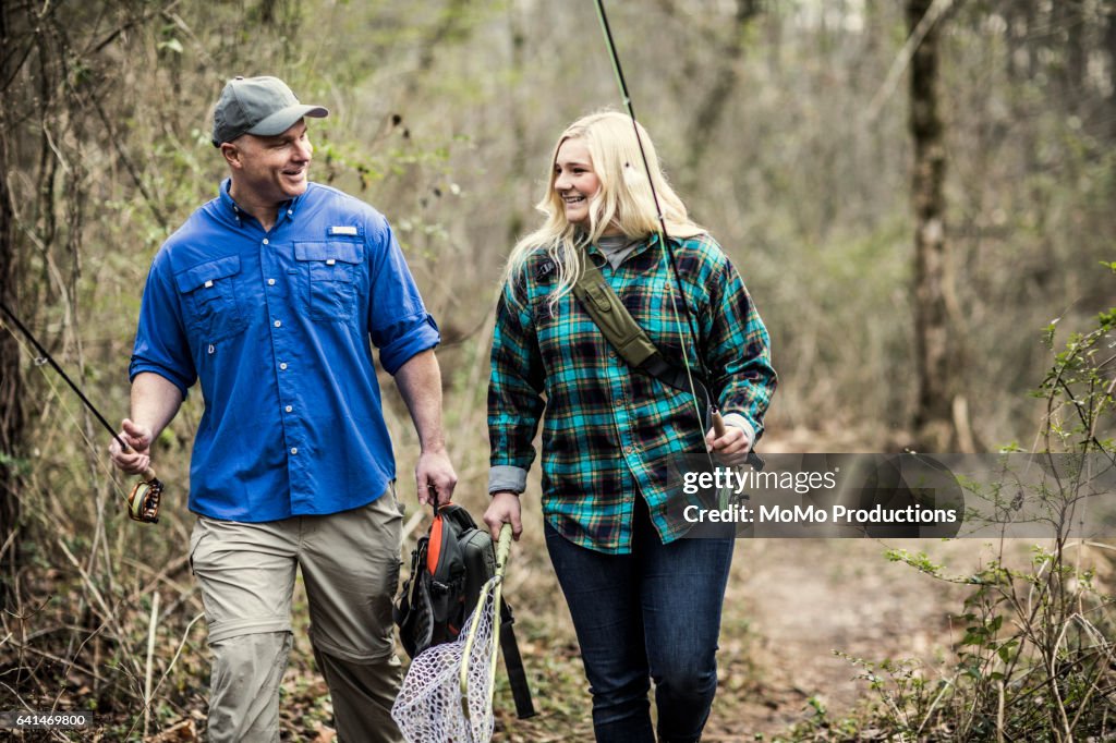 Father and daughter walking through woods with fishing rods