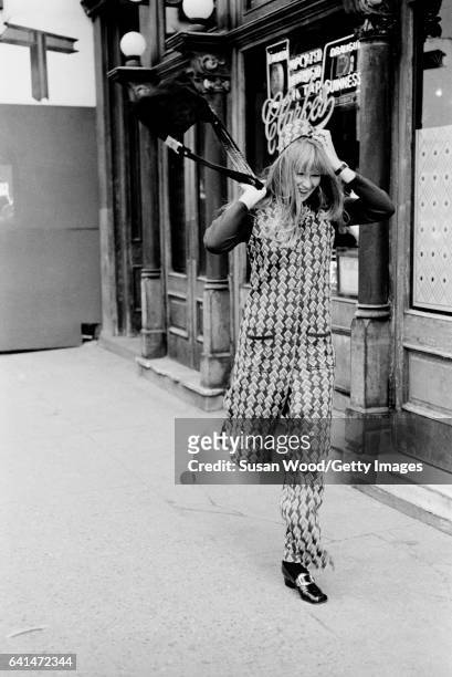 Portrait of an unidentified model, dressed in a matching brocade trouser suit and hat, as she poses in front of PJ Clarke's saloon , New York, New...