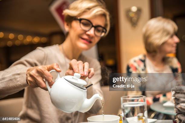 erwachsene frau einen tee in eine tasse gießen - nachmittagstee stock-fotos und bilder