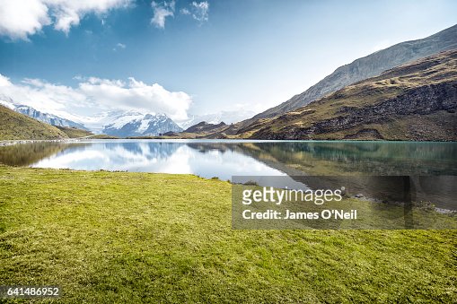 Grassy patch next to lake with mountain reflections