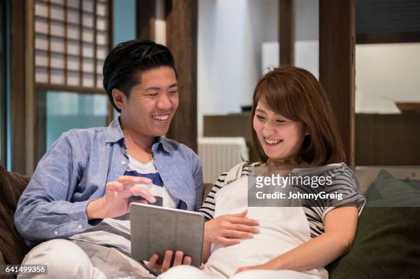 japanse paar met behulp van tablet pc, zwangere vrouw met hand op buik - mid adult couple stockfoto's en -beelden