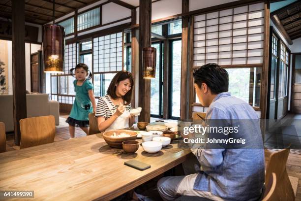 日本語親はバック グラウンドで娘の食卓の前に座って - japanese family ストックフォトと画像