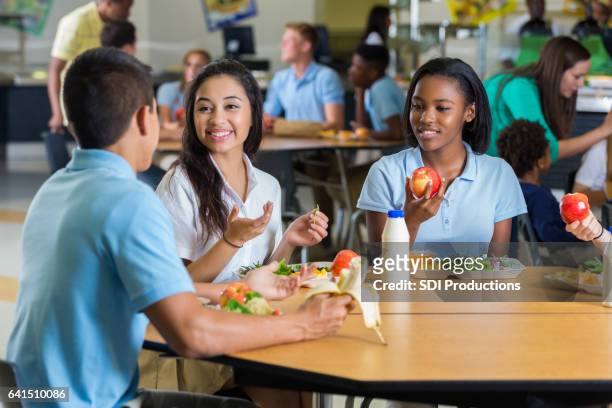 diversos amigos adolescentes comen su almuerzo en la cafetería de la escuela - comedor fotografías e imágenes de stock