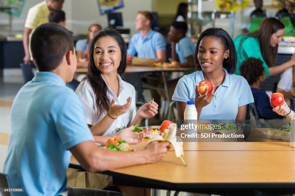 Diverse teenage friends eat lunch in school cafeteria