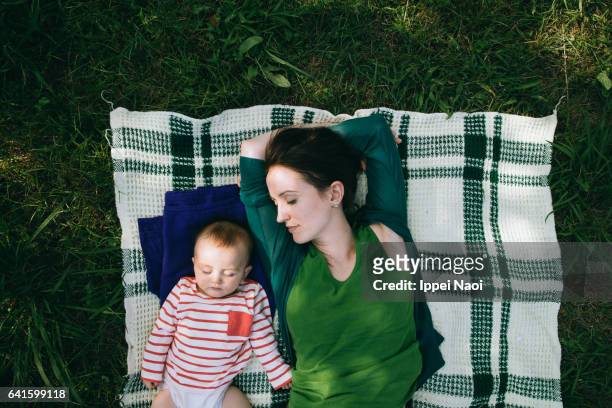 mother and baby having a nap together on lawn - baby sommer stockfoto's en -beelden