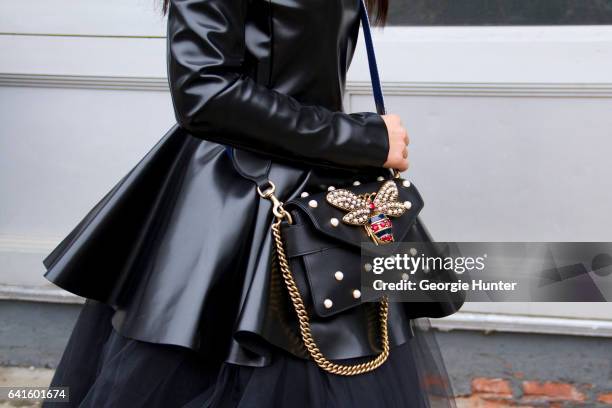 Guest is seen at Spring Studios outside the Lacoste show wearing black patent dress with large under skirt and black bag studded bag with jeweled bee...