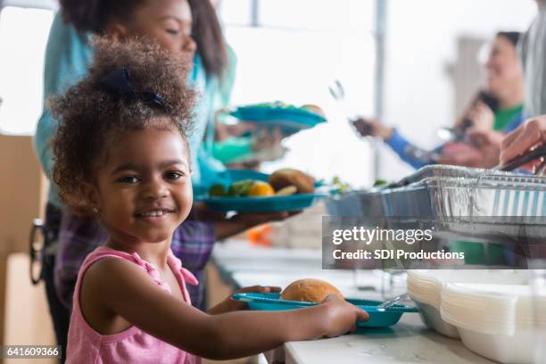 beautiful little girl smiles while receiving meal in soup kitchen - insegurança alimentar imagens e fotografias de stock