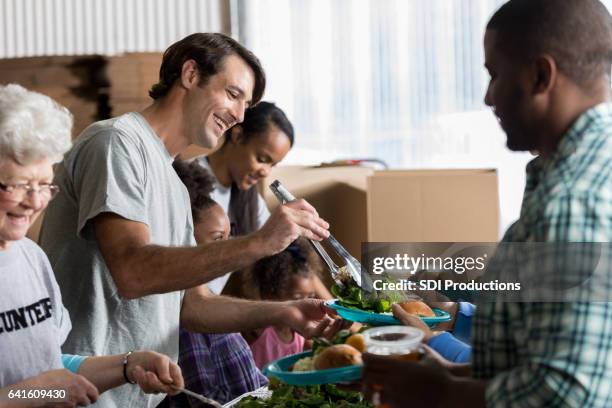 cheerful caucasian man serves healthy meal in soup kitchen - dinner with a cause stock pictures, royalty-free photos & images
