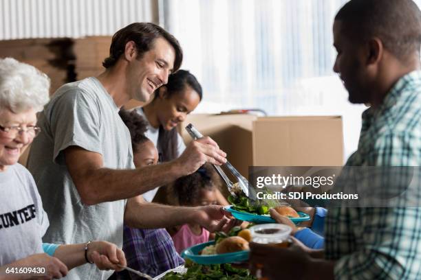 cheerful caucasian man serves healthy meal in soup kitchen - homeless man stock pictures, royalty-free photos & images