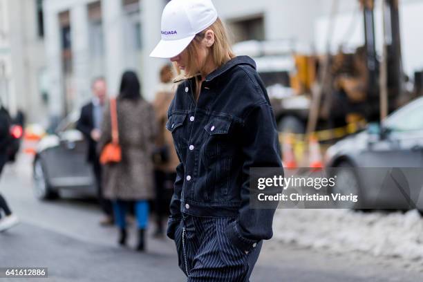 Guest wearing a black denim jacket and white Balenciaga cap, striped pants on February 11, 2017 in New York City.