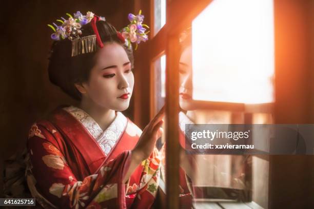 young geisha girl looking through window - geisha japan stock pictures, royalty-free photos & images