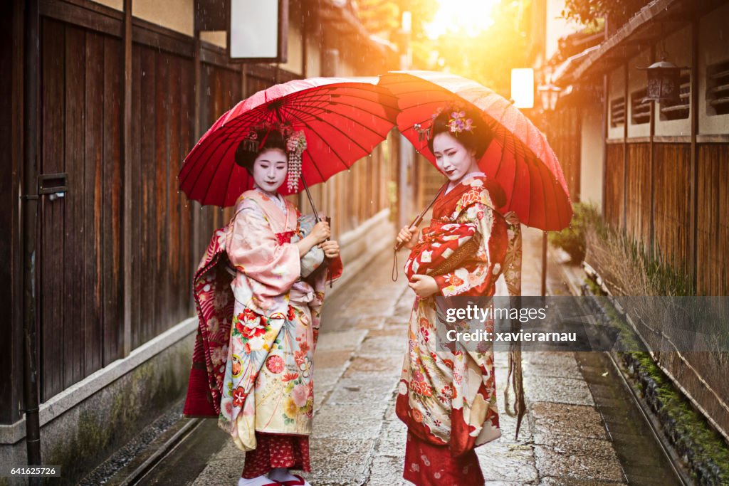 Geisha girls holding red umbrellas on footpath