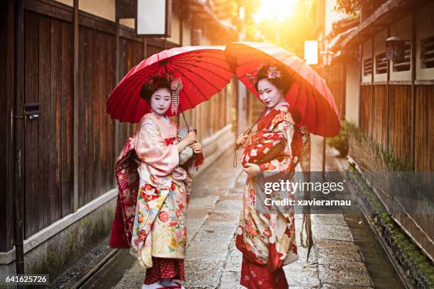 geisha girls holding red umbrellas on footpath - geisha japan stock pictures, royalty-free photos & images