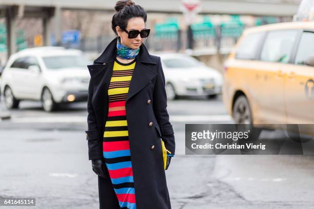 Guest wearing a black wool coat, striped dress outside Lacoste on February 11, 2017 in New York City.
