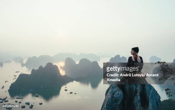 young woman relaxes on rock summit, looks over sea - women in harmony fotografías e imágenes de stock