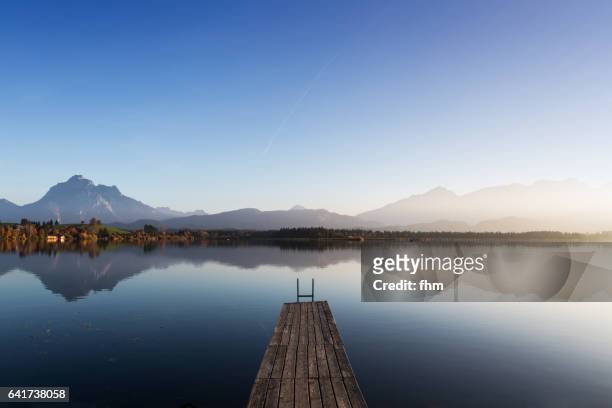 lake hopfen with a jetty and the alps in the background (allgäu/ bavaria/ germany) - bergsteiger stockfoto's en -beelden