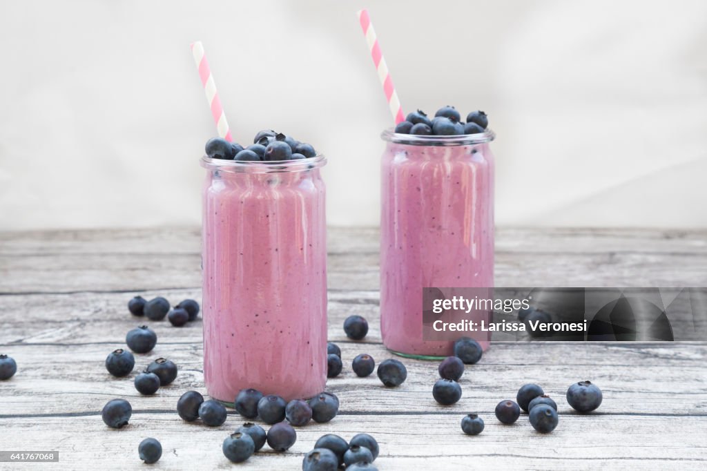 Two glasses of blueberry smoothie and blueberries on wood