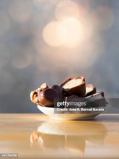 small plate of porcelain with chocolates of chocolate on a table of wood, illuminated by the natural light of the sun - stack of sun lounges stock pictures, royalty-free photos & images