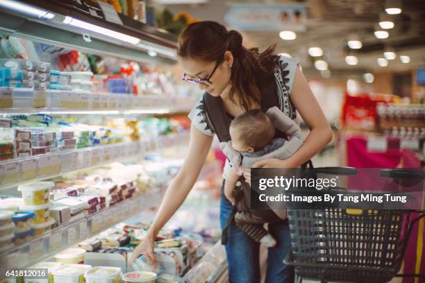 pretty young mom carrying baby in baby carrier while shopping in a supermarket. - shopping candid stock pictures, royalty-free photos & images